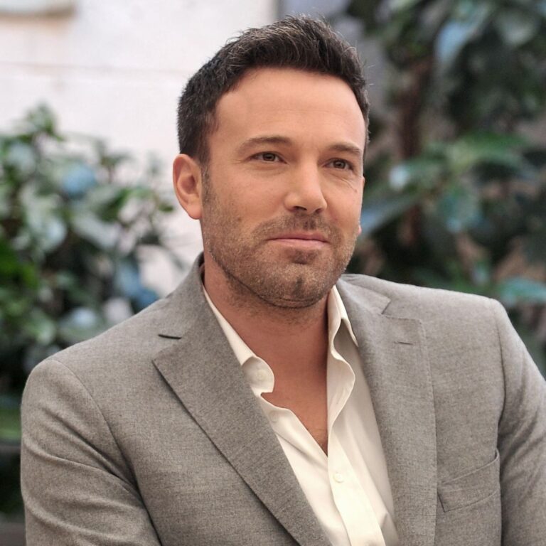 Dressed in a sleek grey suit and crisp white shirt, Ben Affleck exudes timeless elegance with his side-swept haircut.
