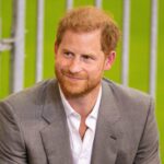 In this delightful photograph, Prince Harry radiates joy, wearing a grey suit and a white shirt, perfectly complementing his polished and well-groomed neat trim haircut.