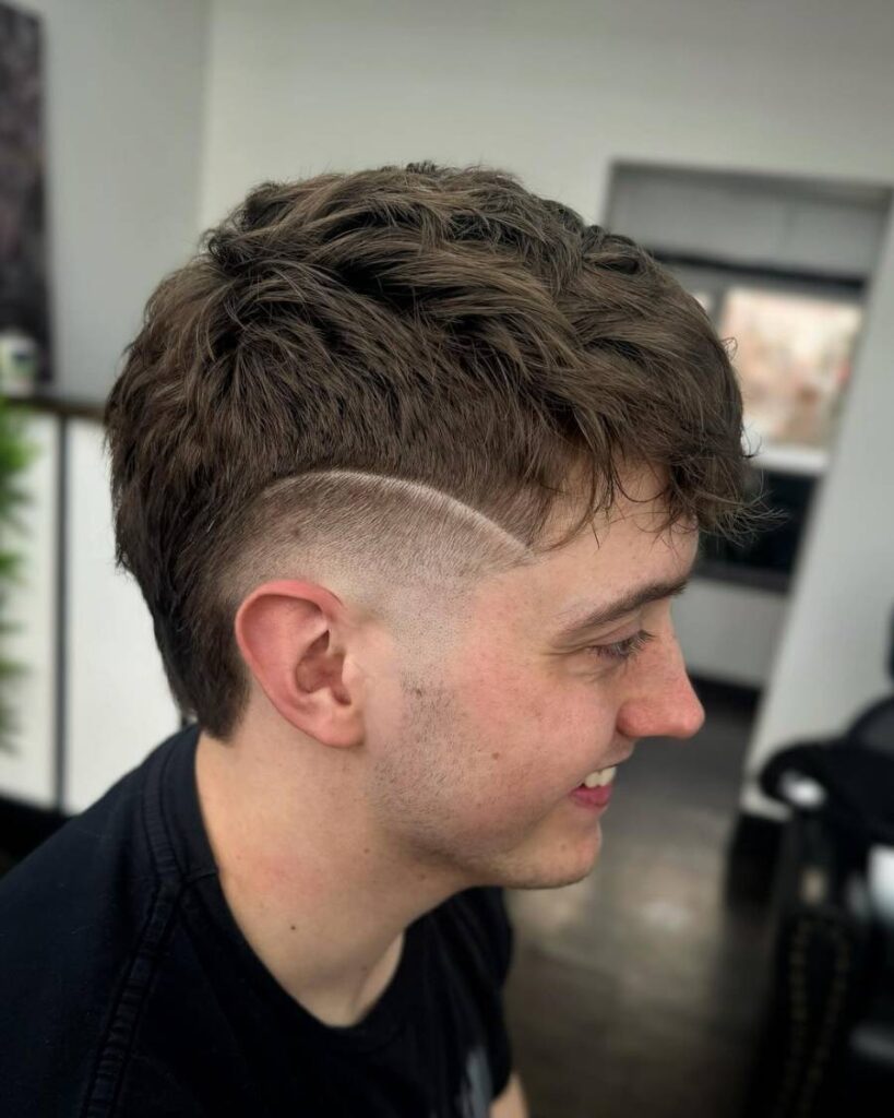 A young man showcasing a stylish burst fade haircut with a shaved undercut, highlighting his modern hairstyle.