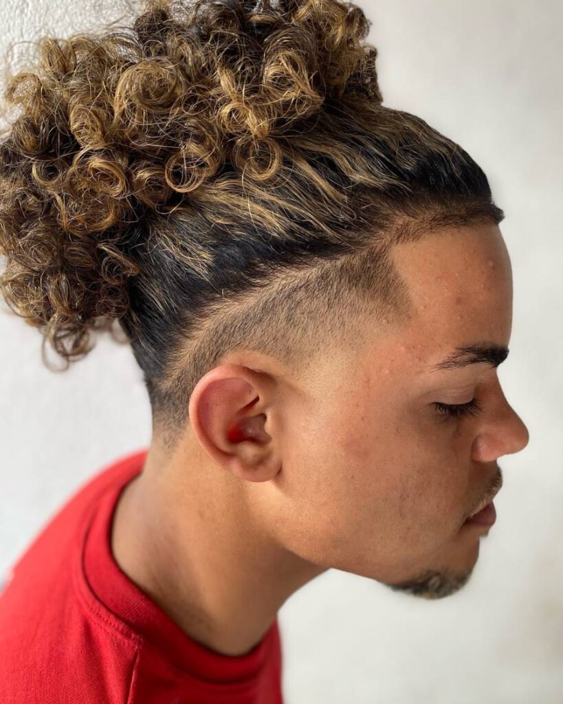 A man with a bun of curly hair complemented by a sleek taper fade haircut.