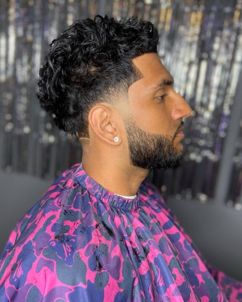 A man with curly hair in a purple shirt, featuring a modern taper fade hairstyle.