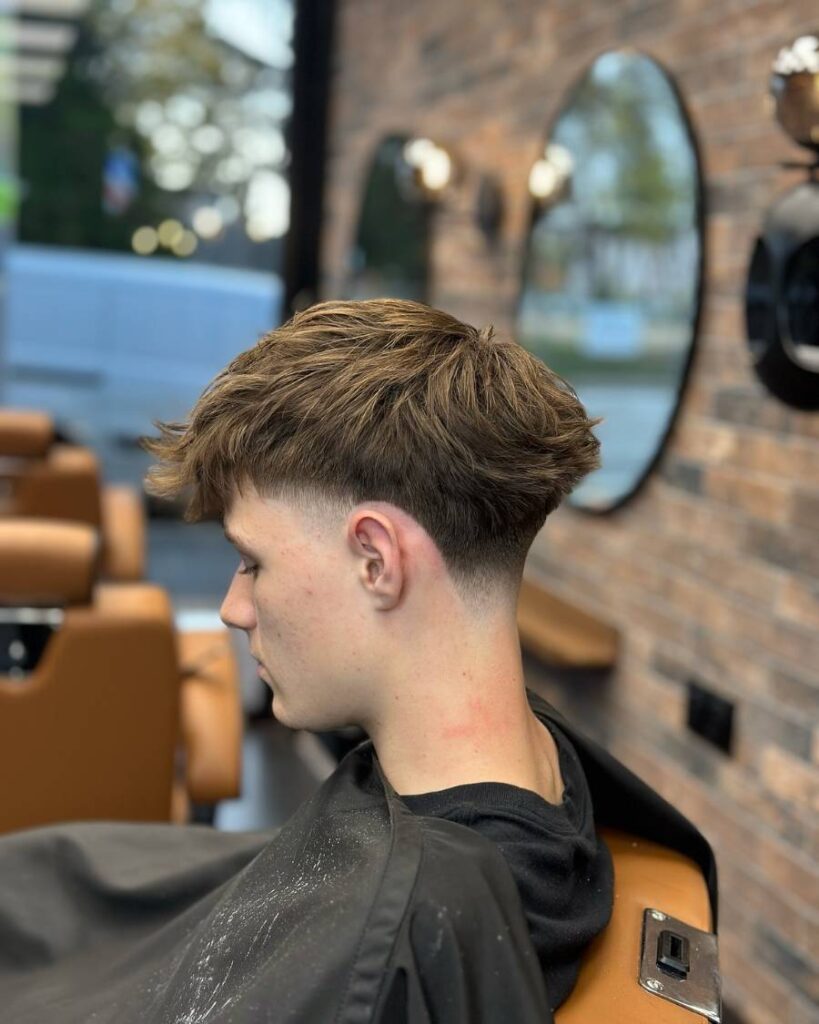 A defined blowout taper style seen from the front with voluminous waves elegantly layered atop the head, converging into a smart taper fade that refines and frames the facial features.