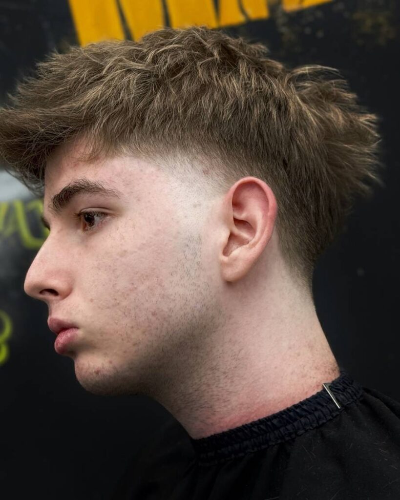 A close-up front view of a blowout taper haircut featuring meticulously tousled waves on top, transitioning into a clean taper fade, accentuating a modern and edgy appeal.